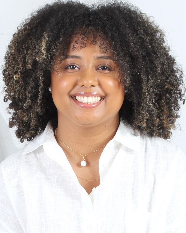 Retrato de Thaís Marcelino, psicóloga, de camisa branca, sorrindo para a câmera.